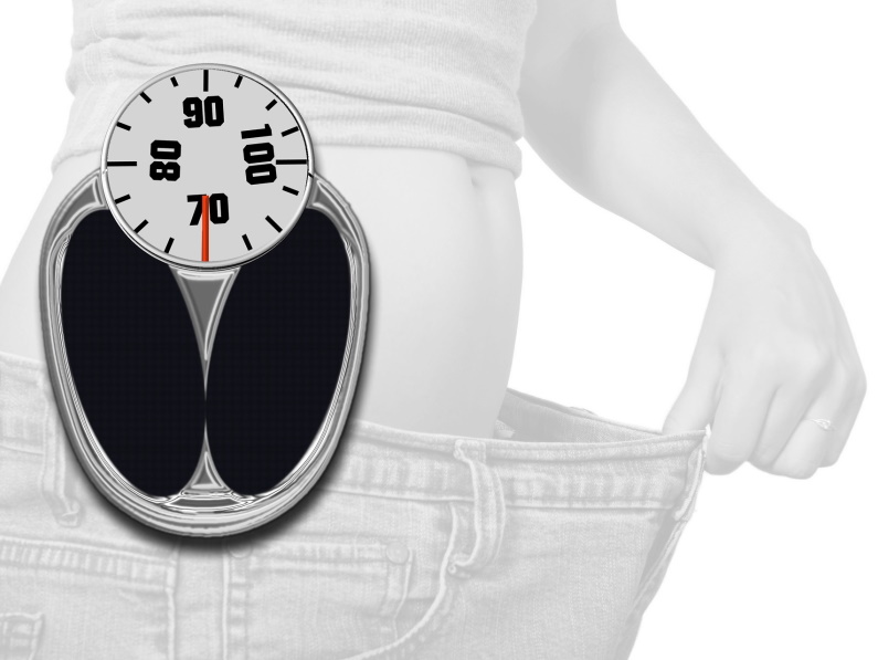 black and white image of someone stretching loose pants over flat abdomen and weigh scale