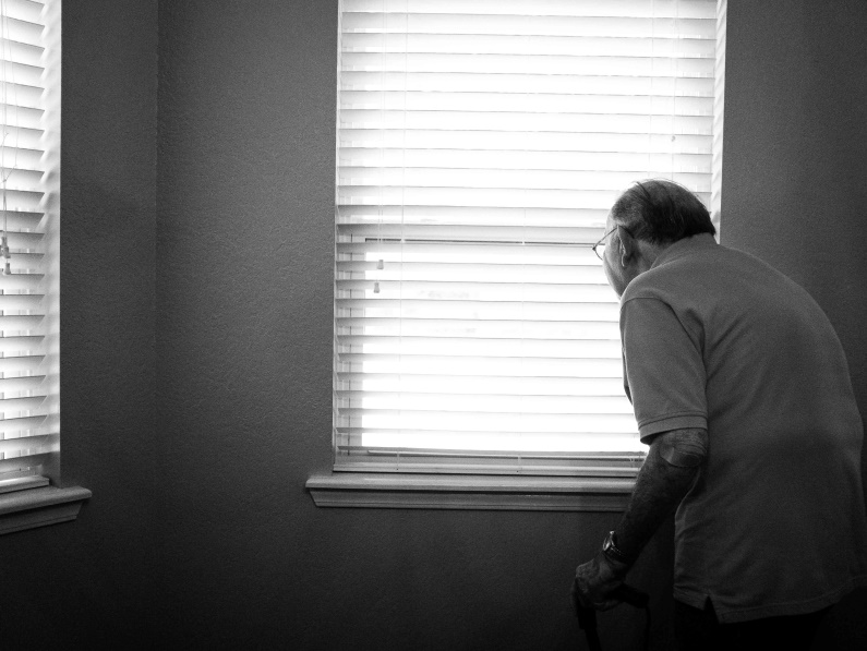 old man standing hunched by window