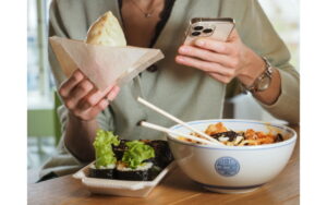 person eating a sandwich and salad, holding their phone