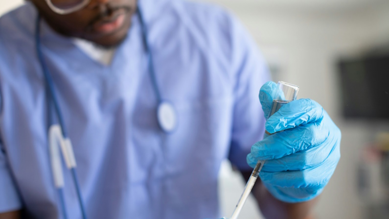 an African American male healthcare worker adding liquid to a lab specimen