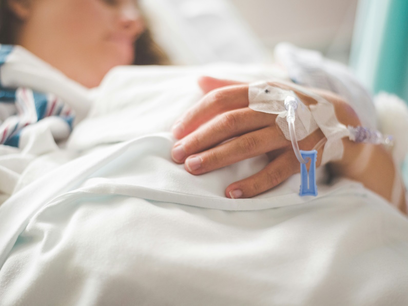 female patient lying in a hospital bed with an IV in her hand.